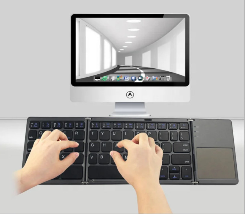 Foldable keyboard being used in front of a computer screen displaying a desktop interface.